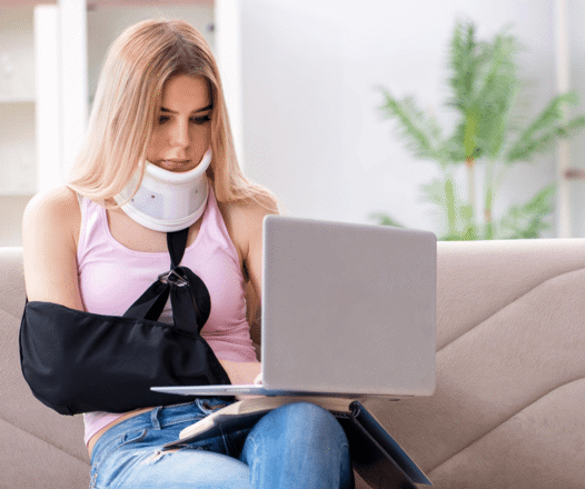 Injured woman, with a shoulder sling and neck brace on her laptop