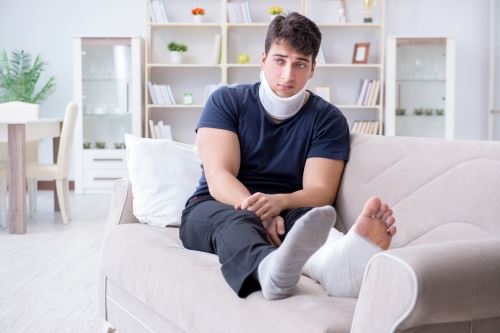 Man sitting on couch with a neck brace and leg in cast from work related injuries